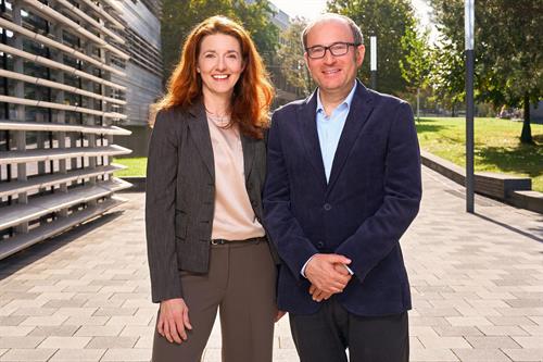 Regine Müller (links) und Konar Mutafoglu (rechts) stehen lächelnd nebeneinander auf dem Campus der Hochschule Düsseldorf. Im Hintergrund sind ein Hochschulgebäude und eine Grünfläche zu sehen. Beide waren bei der DFG-Projektakademie erfolgreich.